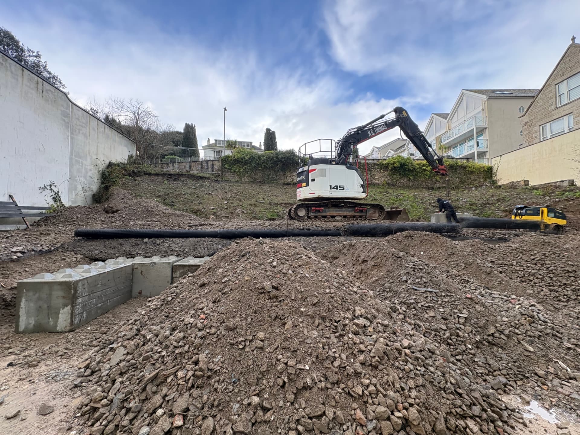 Geogrid reinforcement rolled out across the sloping piling platform with concrete retaining blocks in place