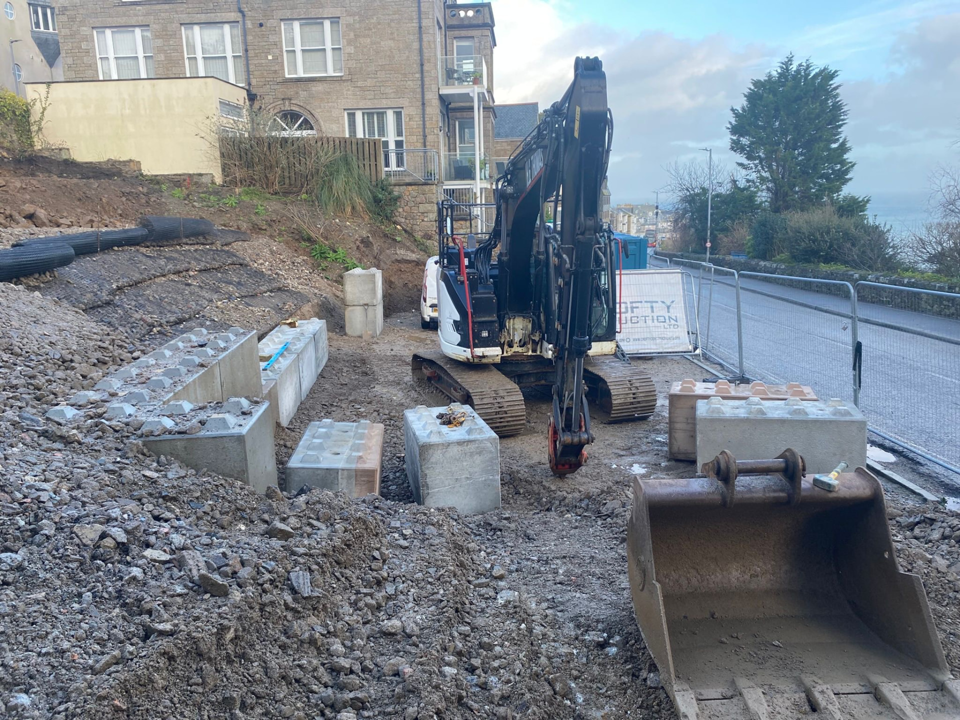 Interlocking concrete retaining blocks and geogrid laid beside the excavator at Elvan House