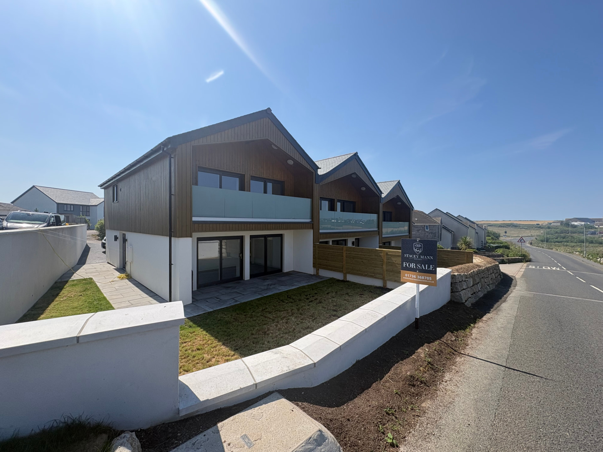 Three completed timber clad passive properties behind a rendered wall on the lane at Sunny Banks, Sennen, Cornwall