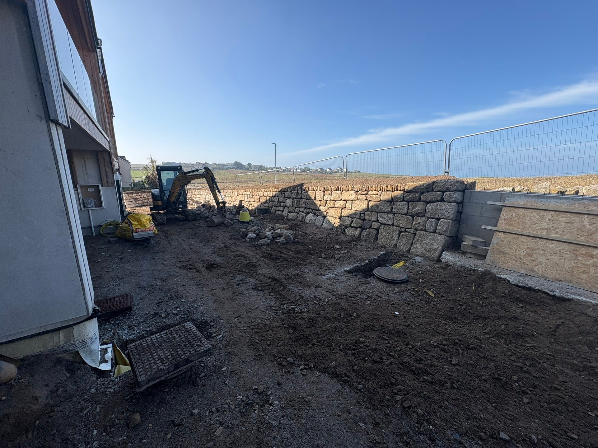 Mini excavator working beside a rebuilt Cornish stone wall at the Sunny Banks site in Sennen, Cornwall