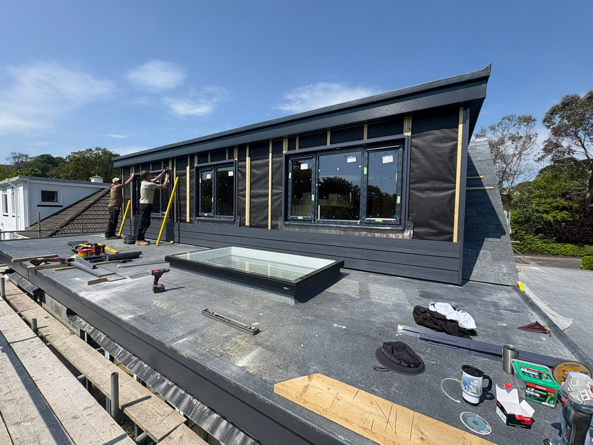 Crofty Construction team fitting dark external cladding around new windows and a rooflight at 3 Polgoon Close in Penzance, Cornwall