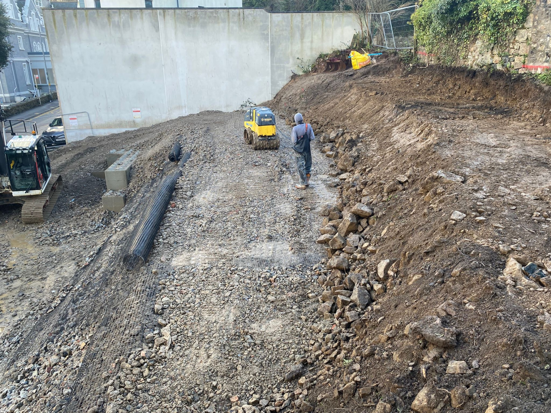 Geogrid rolled out over compacted 6F2 fill with a roller working the sloping piling platform at Elvan House