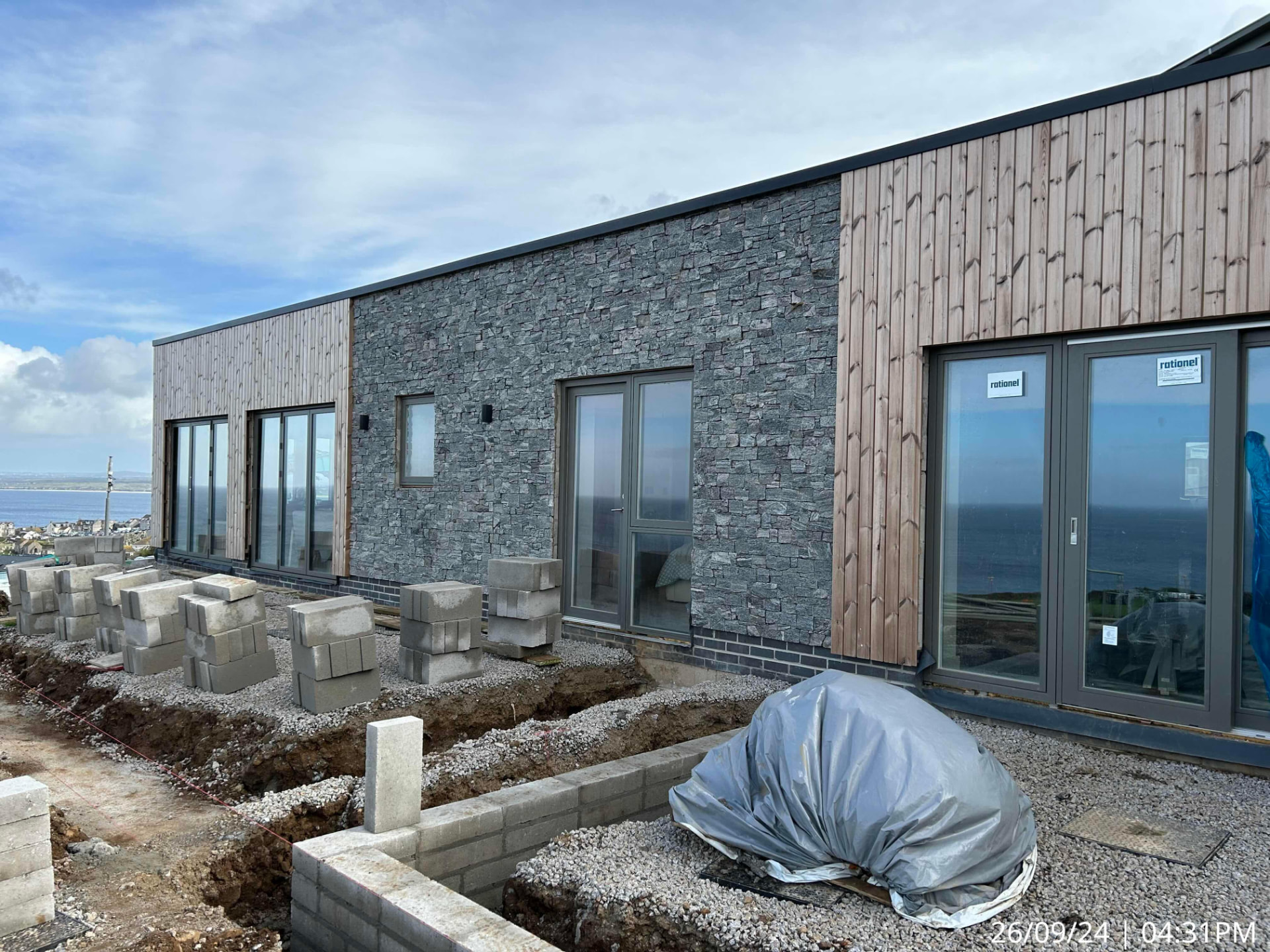Newly clad timber and stone facade of the modern Garrack Hotel apartment building with trenches and blockwork for the external works in St Ives, Cornwall