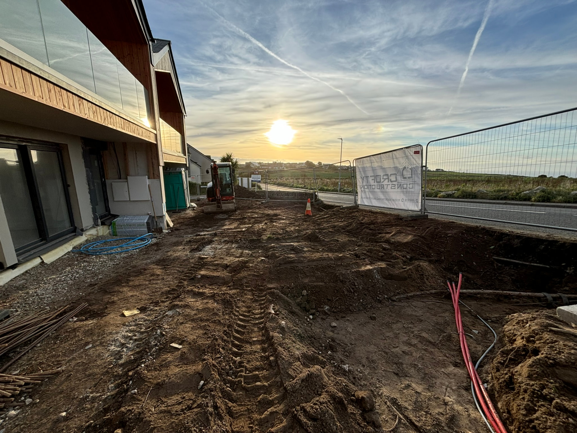 Trenching for services beside the completed timber clad homes with the Crofty Construction site banner at Sunny Banks, Sennen
